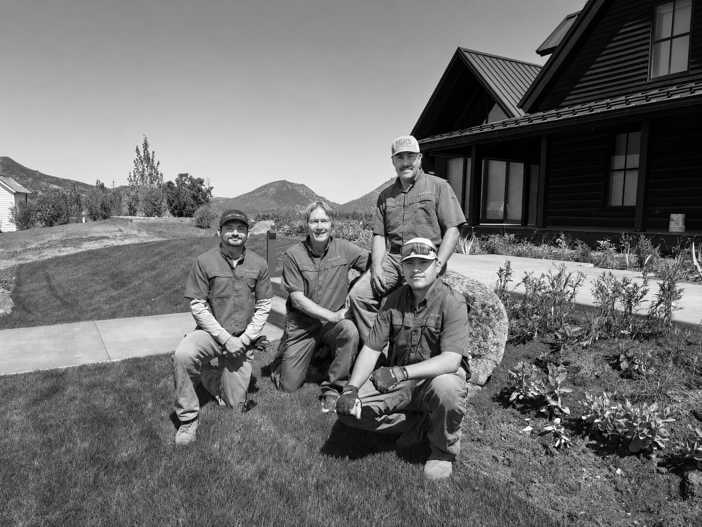 The Escape construction team kneeling on fresh sod beside a newly planted bed at a mountain home